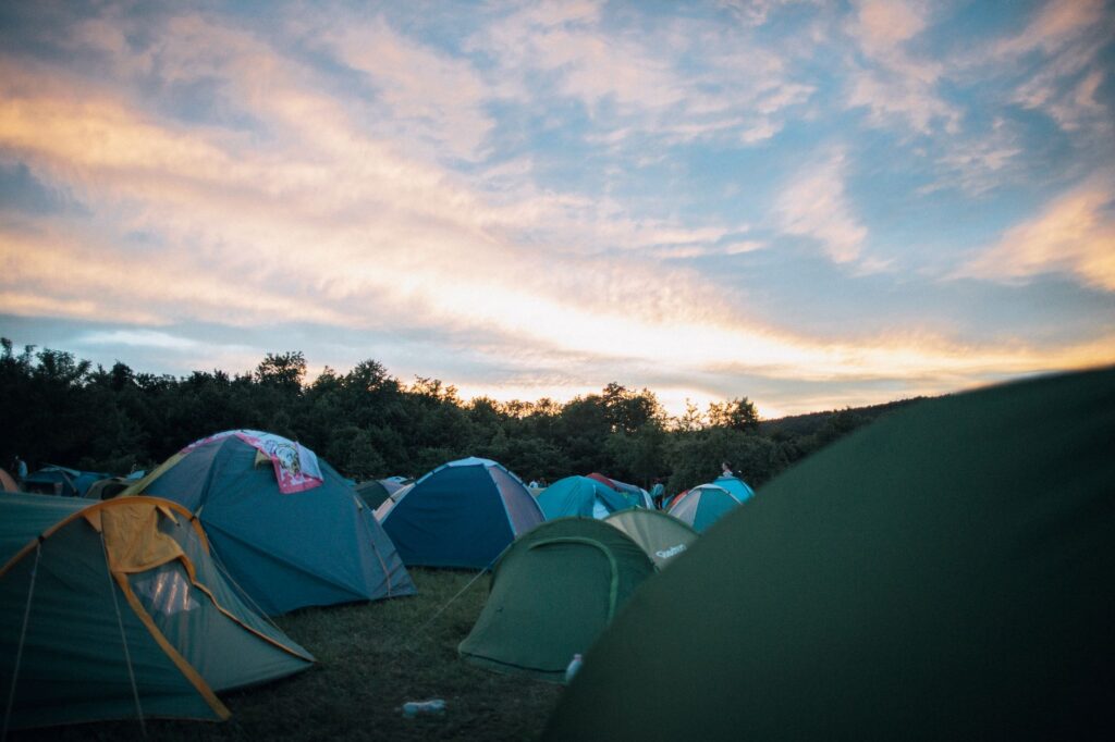 Corturi colorate așezate unul lângă altul în zona de camping a unui festival de muzică, la apus